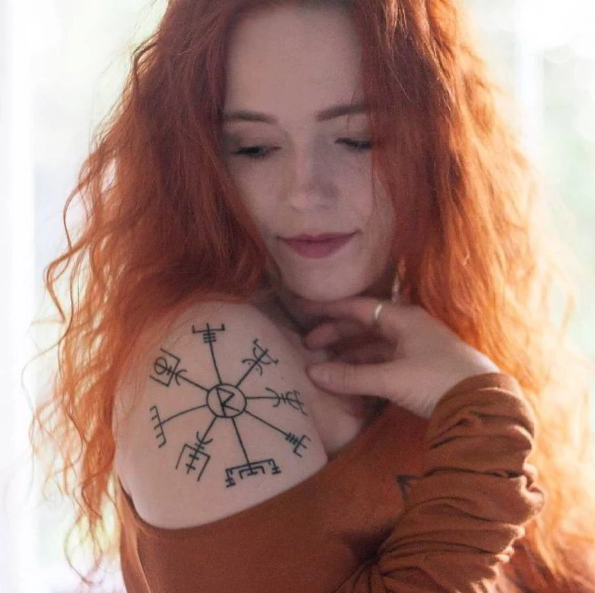 mujer pelirroja con tatuaje de vegvisir en el hombro