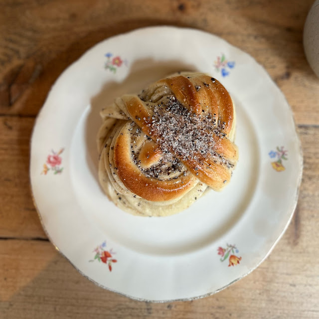 A Swedish bun speckled with cardamon, sitting on a vintage china plate onto of a wooden counter, viewed from above.