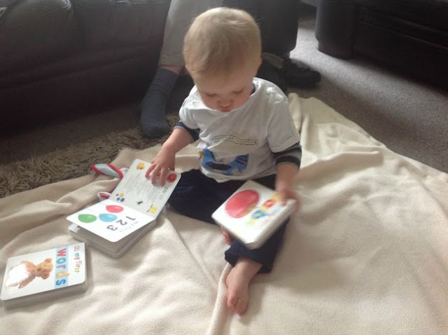 baby on floor with 3 books. abc book in his hand