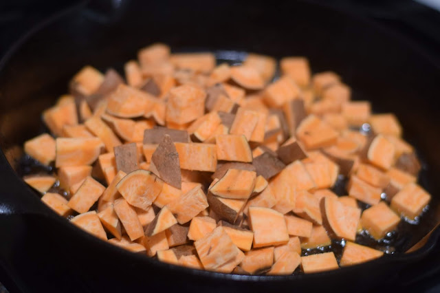 Diced sweet potatoes cooking in a cast iron skillet. 