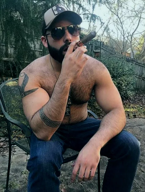 Hairy chested shirtless redneck smoking a cigar wearing a trucker's cap and jeans on the back porch