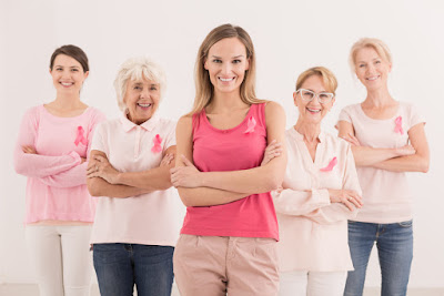 A group of women stand together in support of one another. They are all wearing pink ribbons which symbolize breast cancer awareness. 