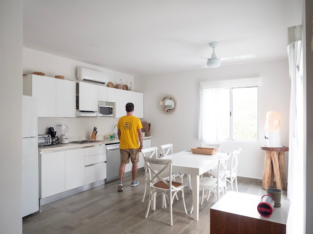 Hombre de espaldas con camiseta amarilla en una cocina muy blanca y luminosa