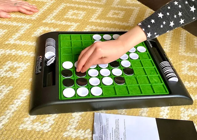 Close up of the Othello game board and a child's hand turning pieces over.