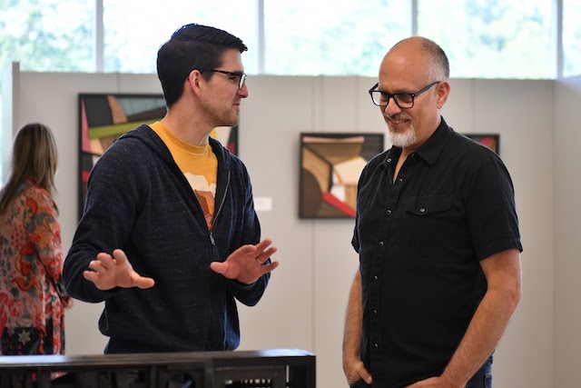 Two men talking about a wooden art piece