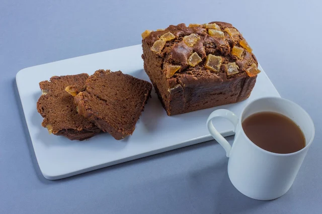 A ginger cake loaf partially sliced and a cup of tea