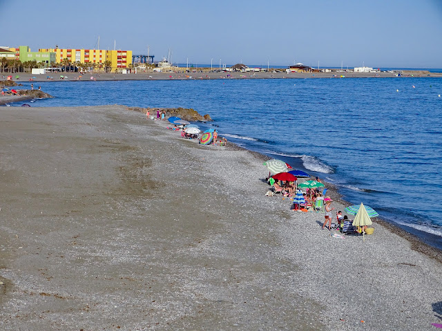Playa de arena con sombrillas y turistas en la orilla con el mar a su frente