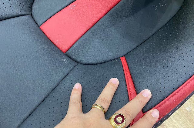 The image depicts a leather seat sample undergoing quality inspection of the stitching and threadwork during the manufacturing process.