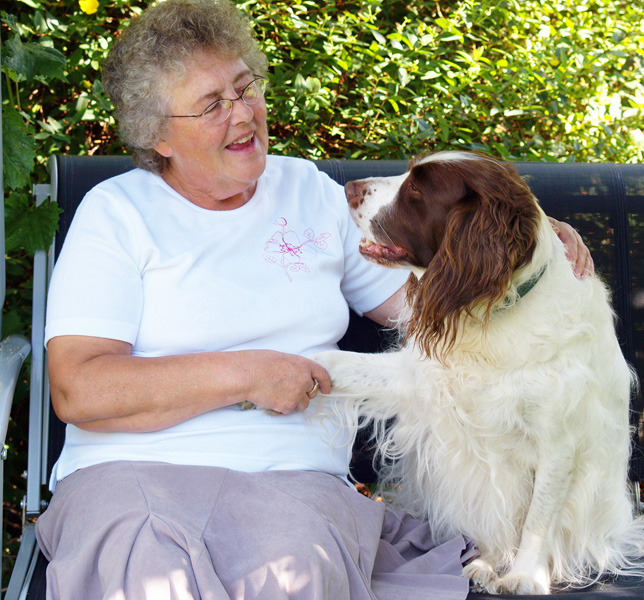 An older woman shakes paw with her spaniel