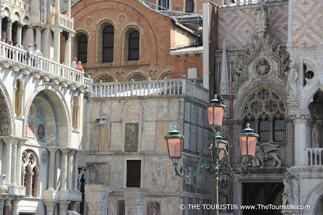 Six people in the sunshine of a white ornamented balcony surrounded by facades in Venetian Gothic Style