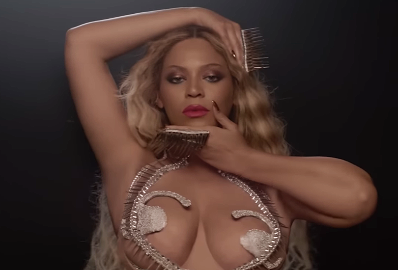 Beyoncé wearing a silver bejewelled bikini top, as she poses with her hands around her face.