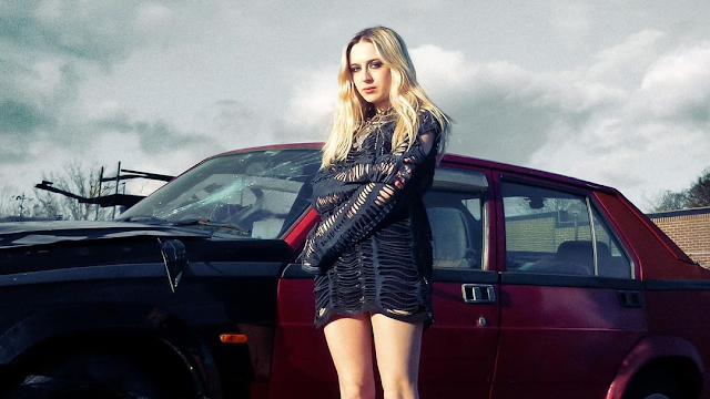 Lizzie Esau in a black dress standing in front of a red car