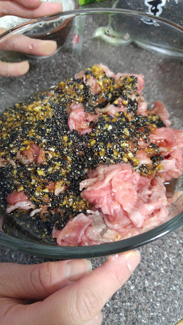 marinating bulgogi meat with black sesame, soy sauce and other ingredients in a glass bowl