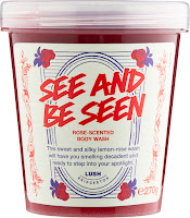A cylindrical clear plastic tub containing thick red raspberry jam like body wash with a yellow and white label with flowers printed on it with see and be seen in red font with lush body wash in black font on a bright background