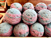 A wide angled photo of a group of spiracle, creator/astroid, inspired, silver, roster coated bath, bombs in a large, light, brown, rectangular box on a bright background