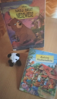 Zdjęcie wystawka biblioteczna malutki biało czarny mis siedzący przy stojaku z książką o niedźwiedziach obok leżąca książka o niedźwiedziach