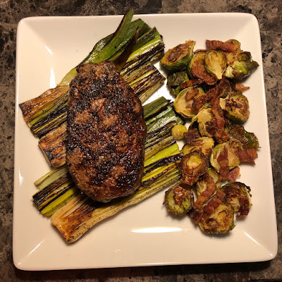 USDA Prime ribeye grilled rare with grilled leeks and bacon roasted Brussel sprouts