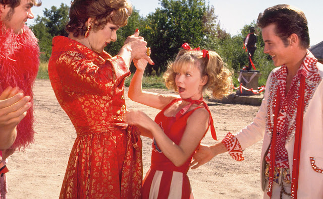 A film still from To Wong Foo. A drag queen is holding a woman's hand.