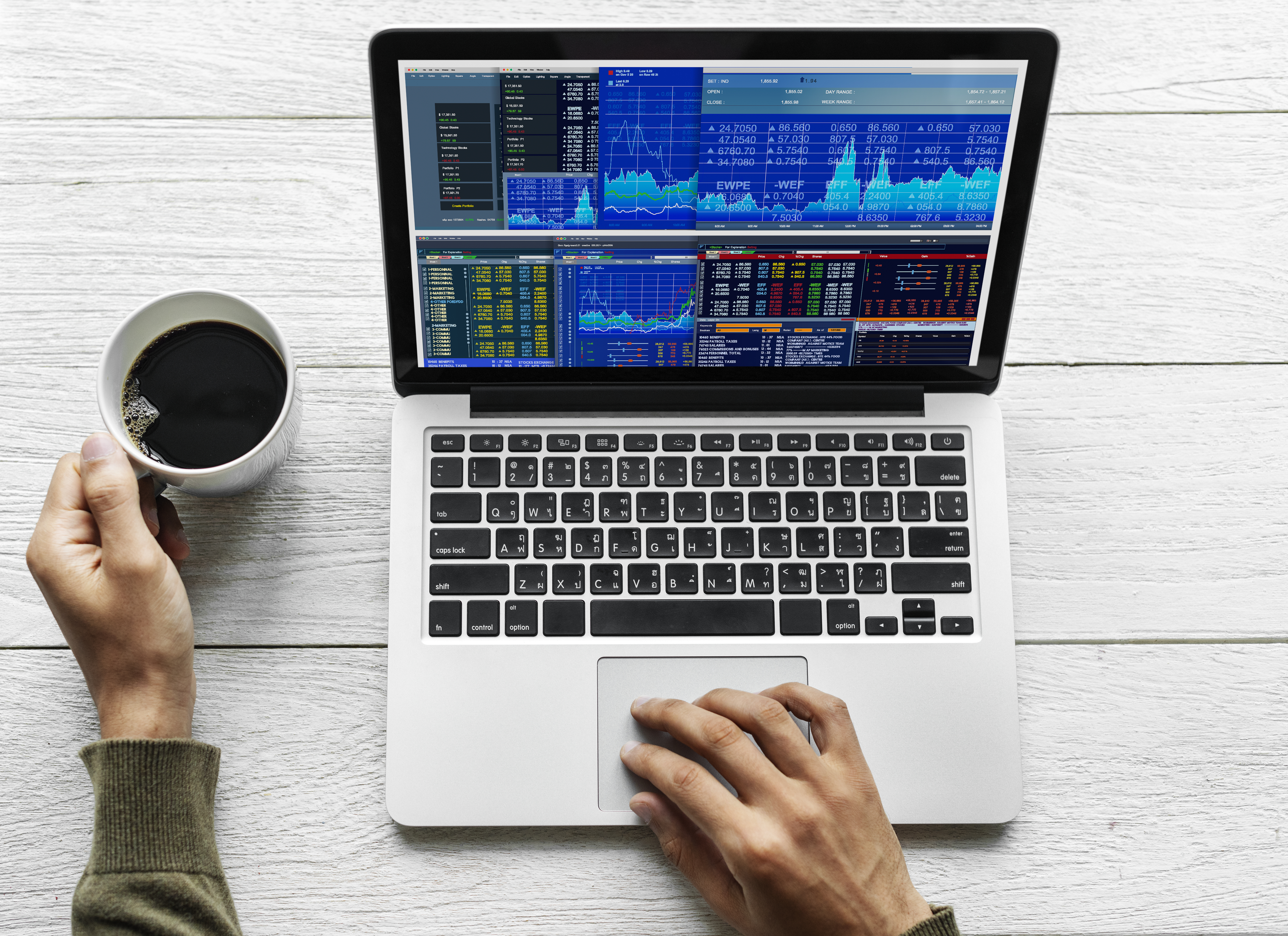 A man uses stock trading app on a grey Macbook Pro while drinking coffee on the table