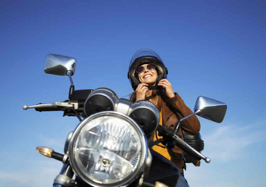 Imagem mostra mulher sorrindo sentada em uma moto.