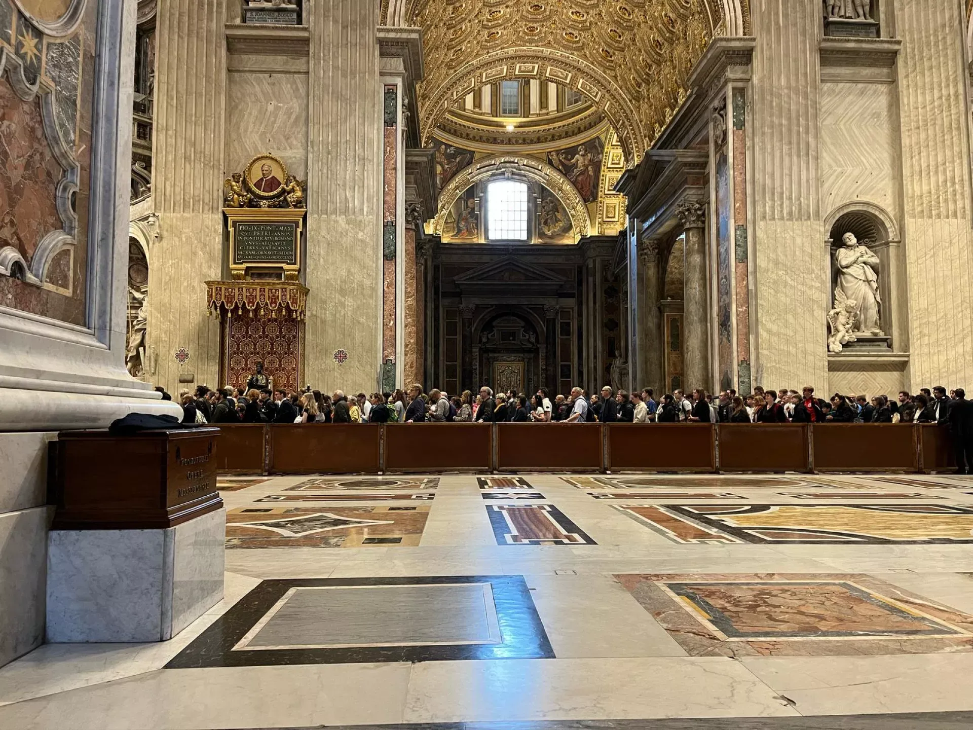 Visão interna da Basílica de São Pedro, com visitantes para se despedir do papa Francisco apreciando a arquitetura impressionante e a arte sacra do local histórico.