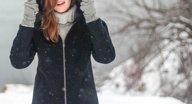 雪の降る屋外で、コート、手袋、毛糸の帽子などを身に着けている女性