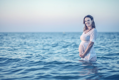 Picture of happy, pregnant a woman standing in the bay. Swimming during pregnancy is ok.