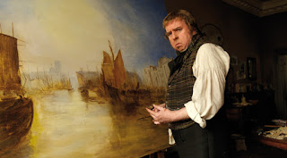 Still from the film Mr Turner - Timothy Spall as JMW Turner standing in front of a painting of ships