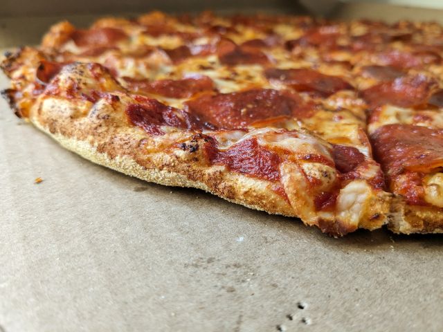 A crust edge of Domino's Extra Large Pepperoni New York Style Pizza.