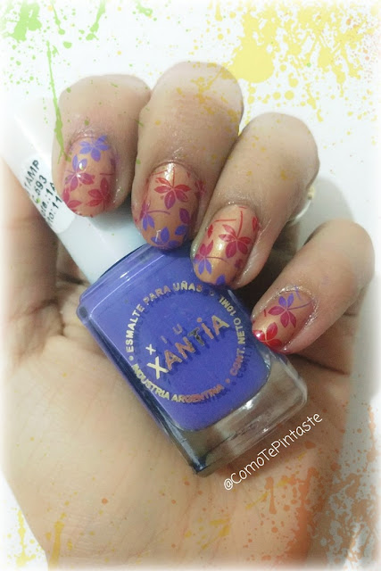 mano con base dorada y flores violetas y rojas sosteniendo esmalte xantia