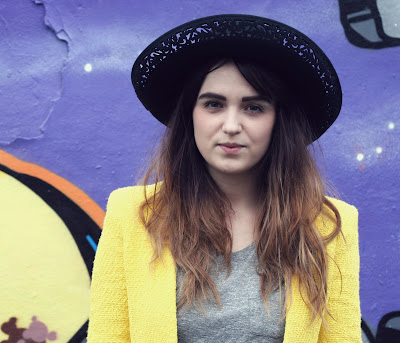 uk fashion style, yellow blazer from zara, grey all saints tee, black leather look verne ashby jeans from all saints styled with white platform wedges and a large brim woolen black hat, chic look with flower sunglasses embellished with black roses. graffiti  wall background 