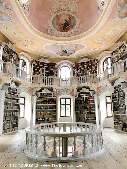Baroque maisonette-style library in yellow and pink pastel colours with white bookshelves and a light wooden floor.