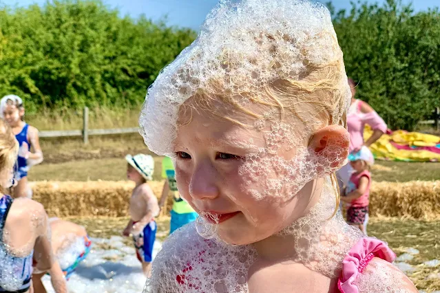 A close up of a child in swimming costume with foam all over her face