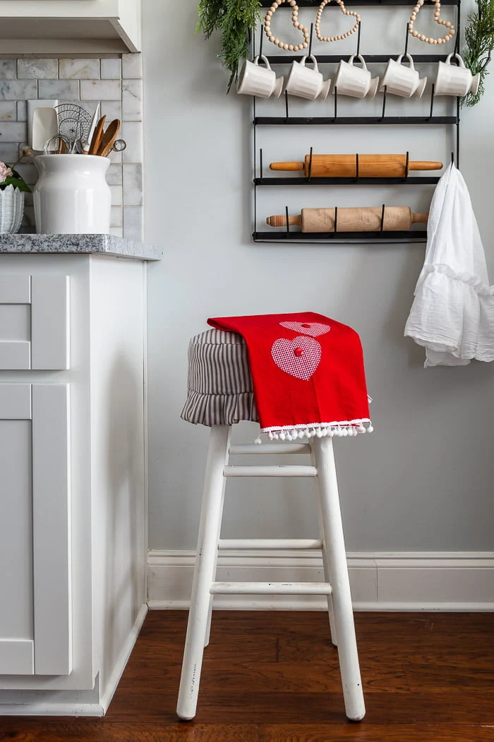 white kitchen, wall mug rack, stool, red Valentines Day tea towel