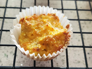 close up of cauliflower tot still in the paper muffin liner. It is yellow in color, with a golden brown top. It has texture in it from the cornmeal.