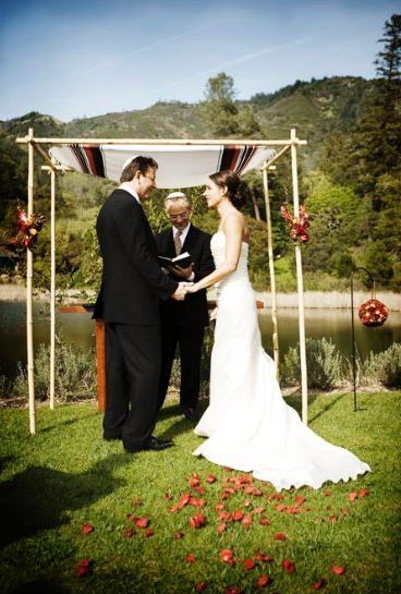 A bamboo Chuppah decorated with traditional fabric and flowers set behind