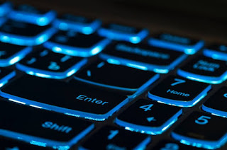 A keyboard enter-key shown with its blue backlight backlit, along with surrounding keys.