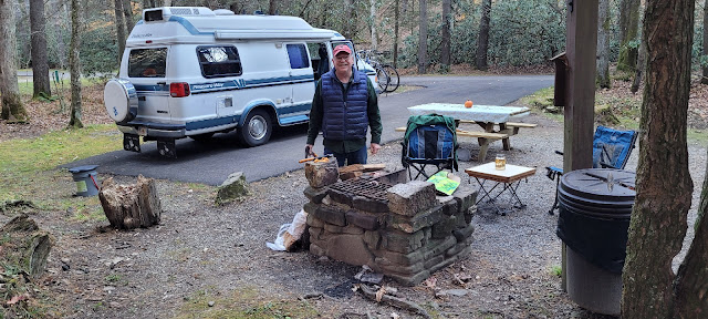 Man in front of stone fireplace with shopped fire wood piled in front of him.