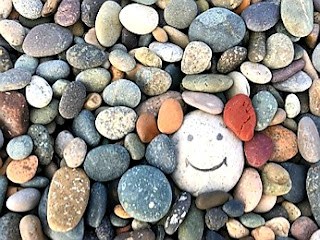 Picture of a Smiling river rock in a sea of colourful faceless smooth river rocks for world kindness week 2023.