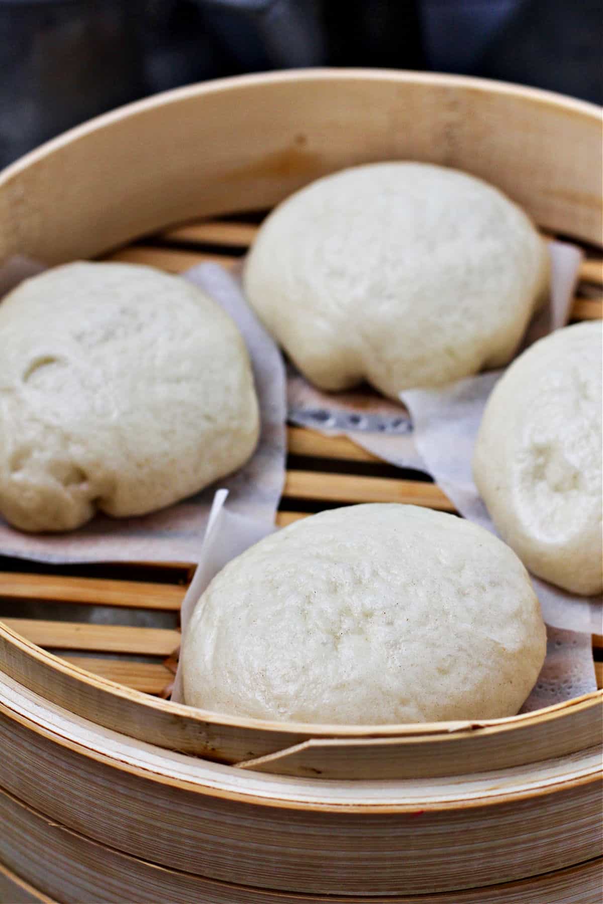 Steamed buns in a bamboo steamer with parchment squares.