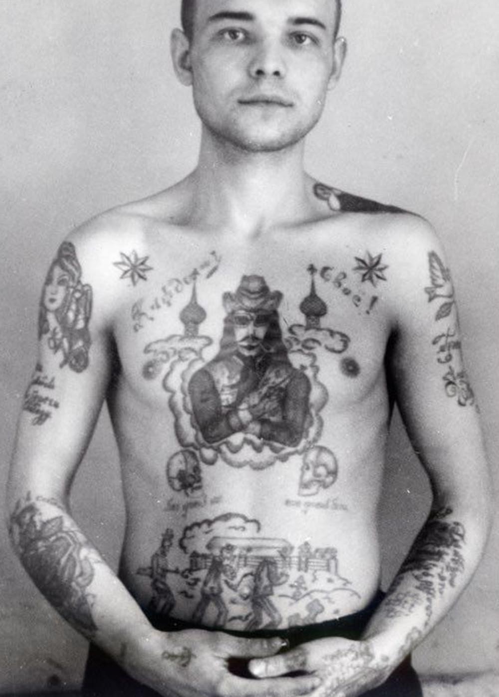 Text on the right arm reads 'Save love, keep freedom.' Text on the left arm reads 'Sinner.' Text across the chest reads 'To each his own.' Text underneath the skulls reads 'God against everyone, everyone against God.' Text on the wrist in German reads 'Mein Gott' (My God). A cowboy with a gun shows this thief is prepared to take risks and is ready to exploit any opportunity. A dove carrying a twig (left shoulder) is a symbol of good tidings and deliverance from suffering.