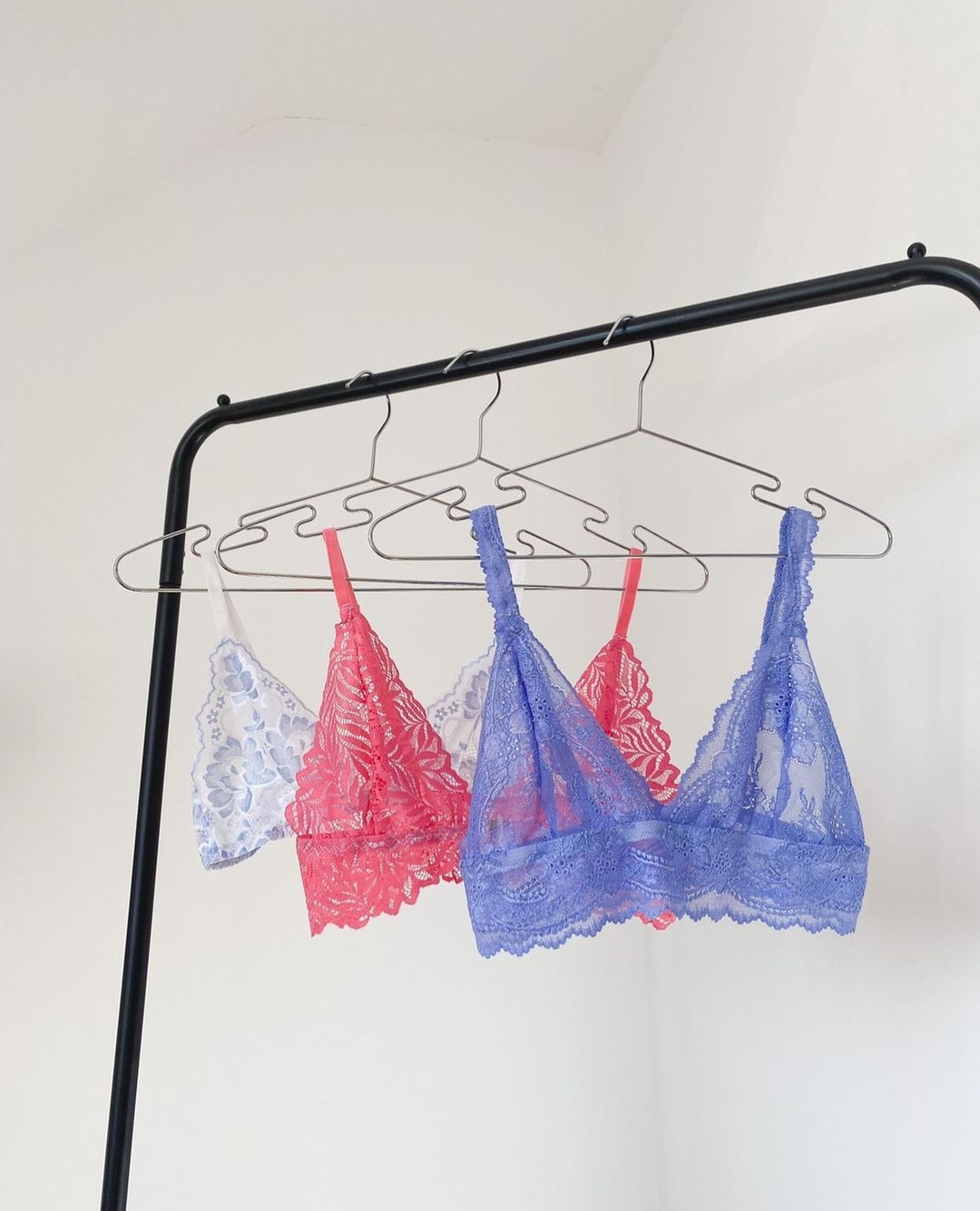 A clothes rail, from which is hanging three hangers each with a different coloured lacy bralet on them - one purple, one peach and one white