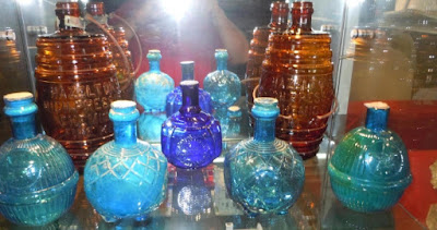 Half a dozen patterned glass balls with necks like a wine or beer bottle's neck. They are various shades of blue. The photo is taken in front of a reflective surface, with the camera's flash visible at the top.