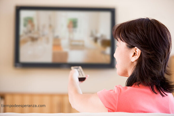 Mujer mirando televisión cambiando los canales con el control