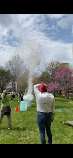 Crowd watches an experiment where water and ducks are propelled out of a trashcan to mimic a volcanic eruption