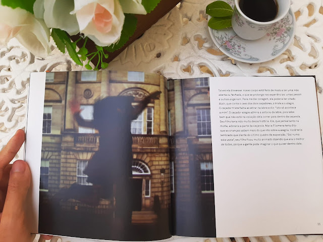 O livro é visto aberto sobre uma mesa branca, onde há também um arranjo de flores e uma xícara de porcelana. Uma mão segura o livro do lado esquerdo. Na página esquerda há uma fotografia mostrando a silhueta de uma mulher em movimento. Sobre ela, é projetada uma imagem de prédios urbanos com arquitetura européia.