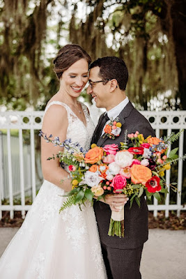 bride holding colorful bouquet with groom next to her in black suit