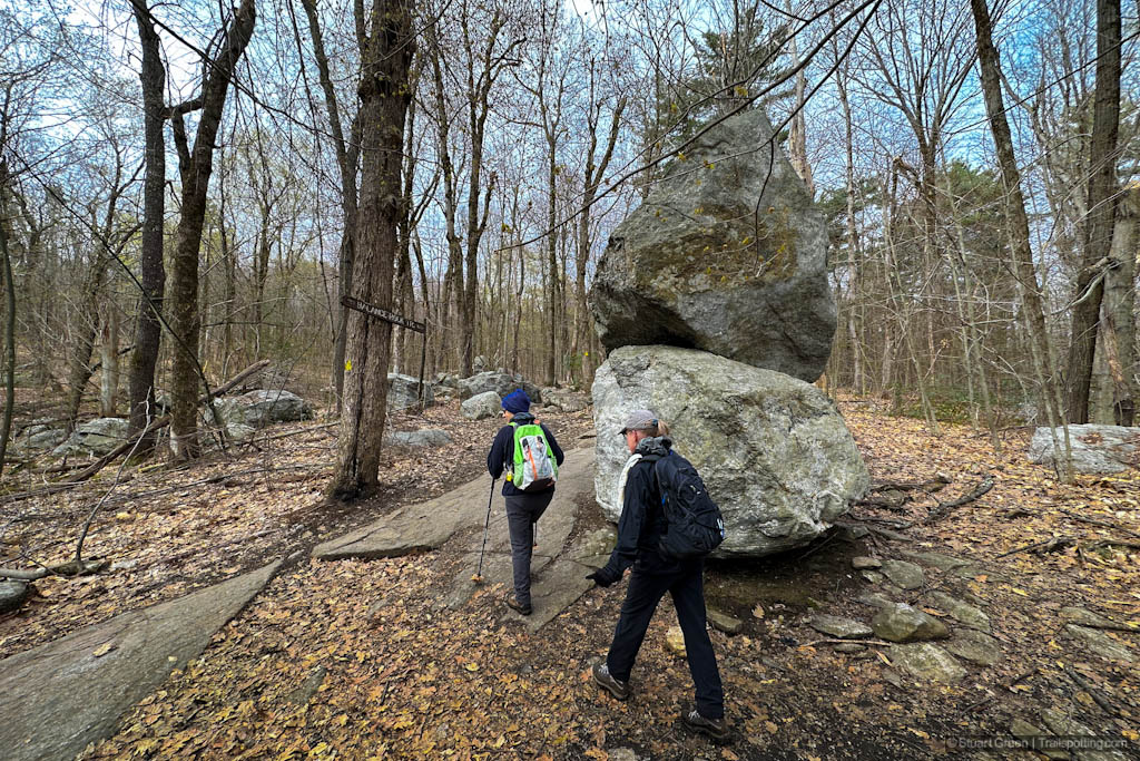 Hikers passing large boulders stacked on each other. Spring season with bare trees and dead orange leaves on the ground