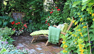A lounge chair with green cushions on a patio surrounded by vegetation.