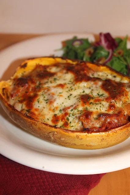 Pepperoni pizza stuffed spaghetti squash on a serving plate with a salad.